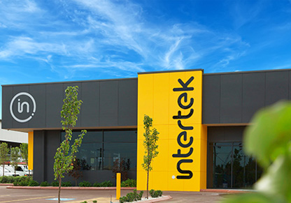 The entrance to the Intertek Minerals Global Centre of Excellence, a dark grey building with a large yellow Intertek sign going vertically down its front. 