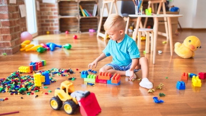 Young caucasian kid playing at kindergarten with toys blocks. Preschooler boy happy at playroom building a tower