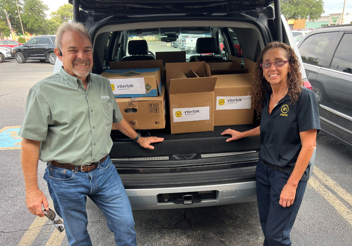 Two Intertek employees stand in front of a car boot full of donated supplies. 